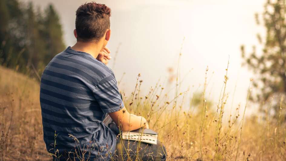 Symboldbild: Ein Mann hält eine Bibel auf dem Schoß und betrachtet die Landschaft Symboldbild: Ein Mann hält eine Bibel auf dem Schoß und betrachtet die Landschaft